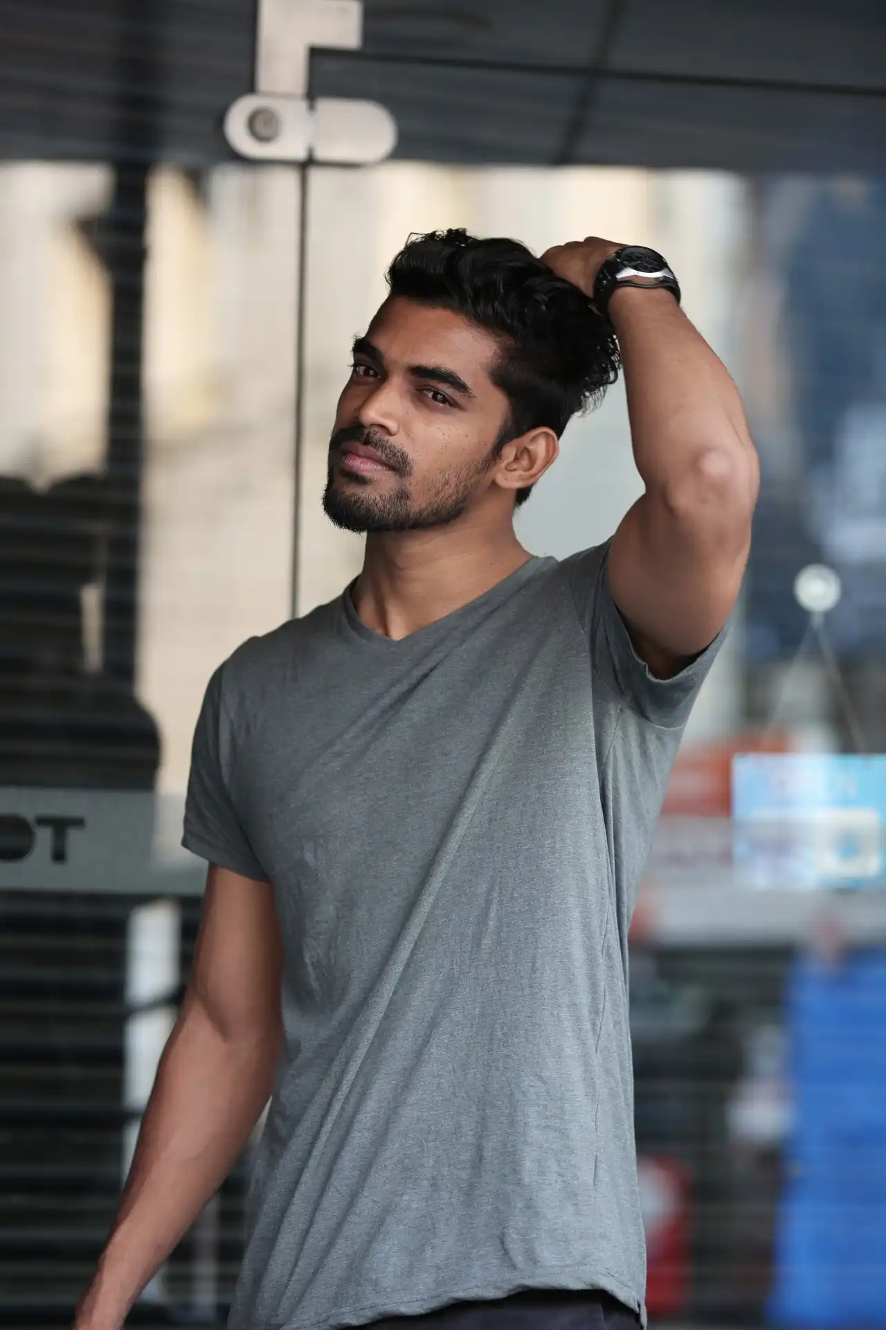 A man with his hand on his head , wearing a grey coloured t-shirt